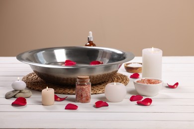 Photo of Bowl of water, rose petals, burning candles and sea salt on white wooden table. Pedicure procedure