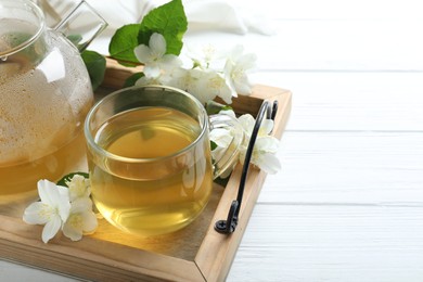 Photo of Cup of tea and fresh jasmine flowers on white wooden table