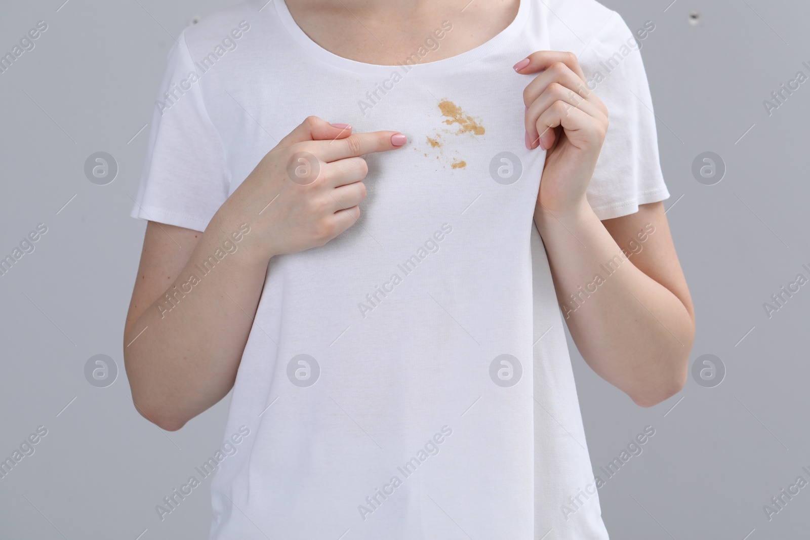 Photo of Woman showing stain on her t-shirt against light grey background, closeup