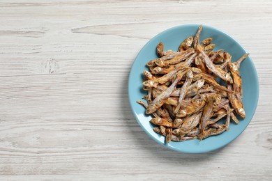 Plate of tasty dried anchovies on white wooden table, top view. Space for text