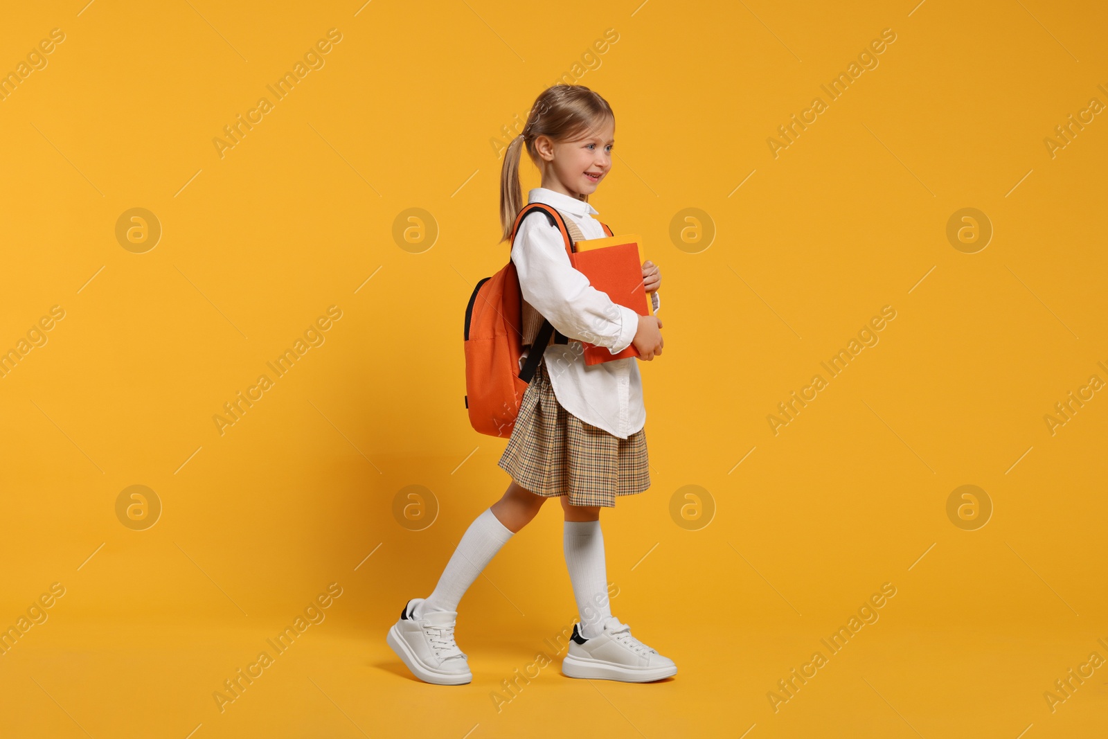 Photo of Happy schoolgirl with backpack and books on orange background