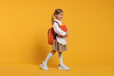 Happy schoolgirl with backpack and books on orange background