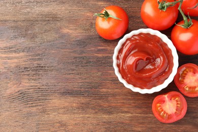 Photo of Bowl of tasty ketchup and tomatoes on wooden table, flat lay. Space for text