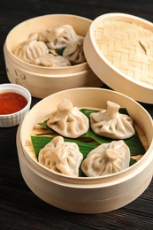 Photo of Bamboo steamer with leaves and tasty baozi dumplings on table