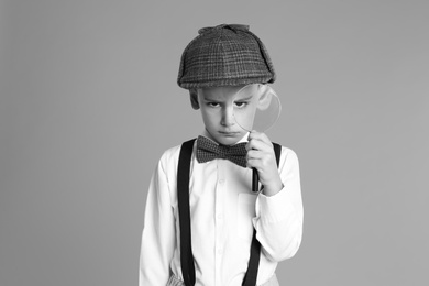Little boy with magnifying glass playing detective on grey background, black and white effect