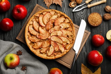 Photo of Delicious apple pie and ingredients on black wooden table, flat lay