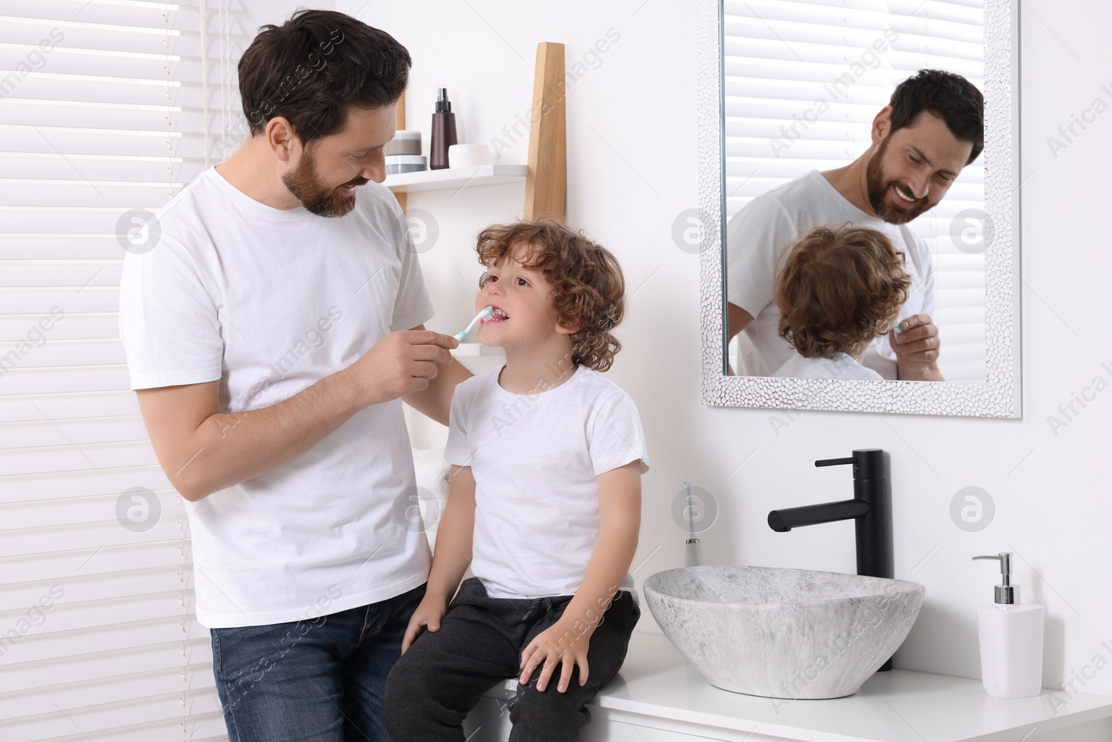 Photo of Father helping his son to brush teeth in bathroom