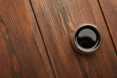 Photo of Soy sauce in bowl on wooden table, top view. Space for text