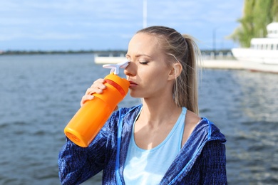 Photo of Woman in sportswear drinking protein shake near river