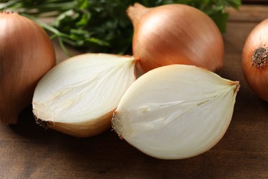 Photo of Whole and cut onions on wooden board, closeup