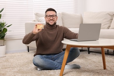 Photo of Handsome man with credit card using laptop for online shopping at home