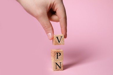 Photo of Woman making acronym VPN with wooden cubes on pale pink background, closeup