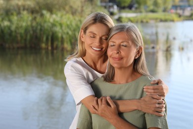 Family portrait of happy mother and daughter hugging near pond. Space for text