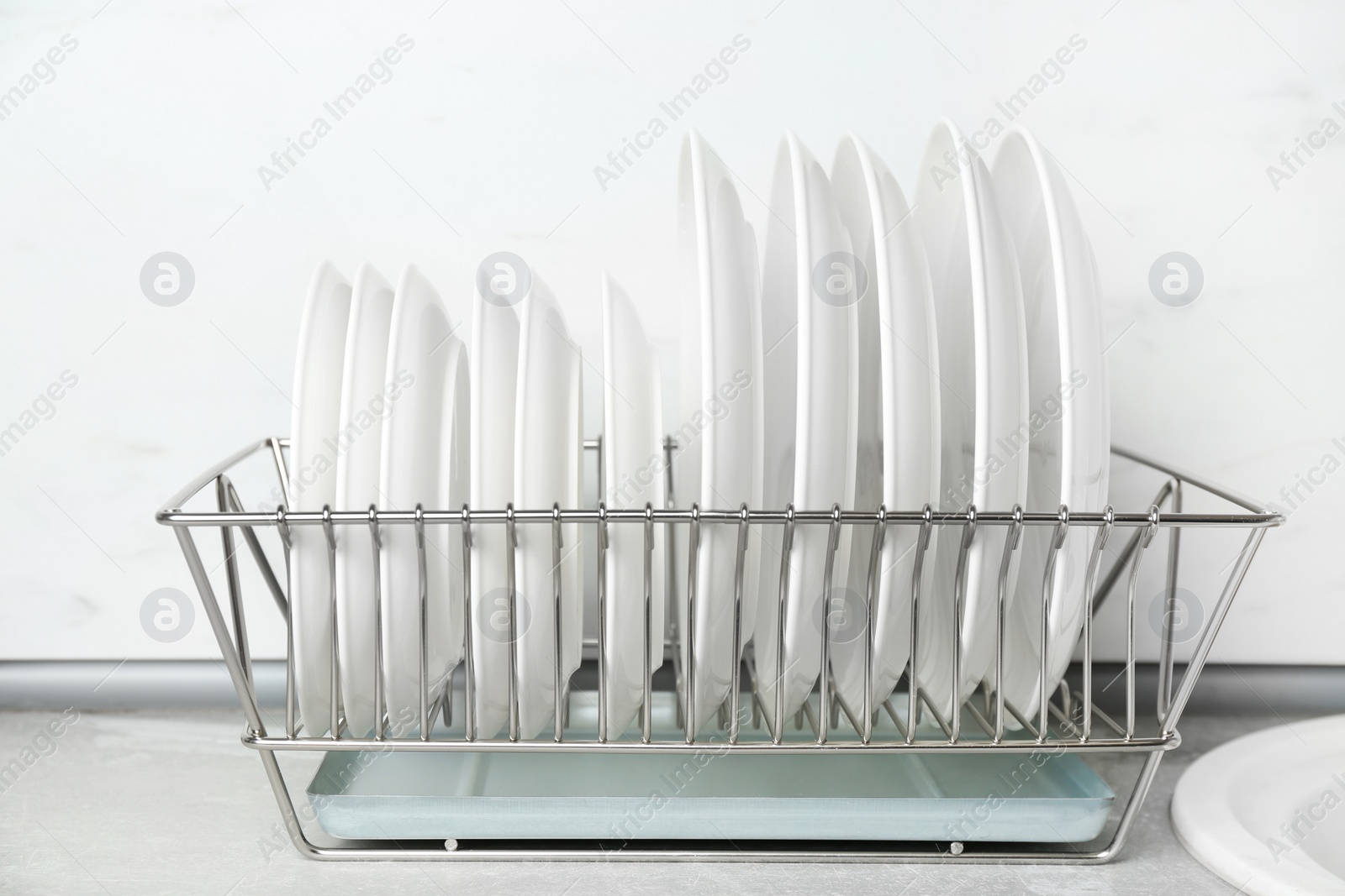 Photo of Different clean plates in dish drying rack on kitchen counter