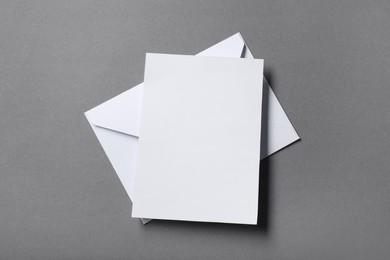 Blank sheet of paper and letter envelope on grey background, top view