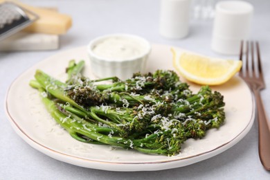 Tasty cooked broccolini with cheese, lemon and sauce on table, closeup