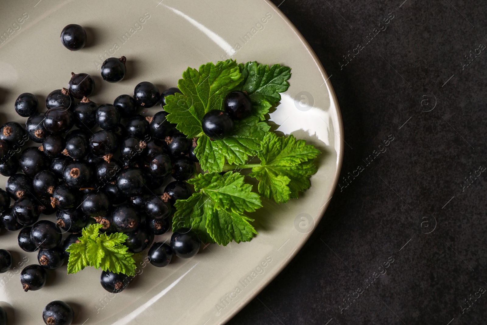 Photo of Plate with ripe blackcurrants and leaves on dark background, top view. Space for text