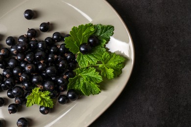 Photo of Plate with ripe blackcurrants and leaves on dark background, top view. Space for text