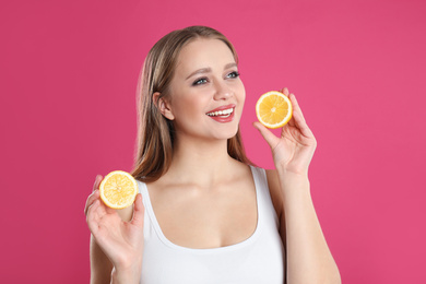 Photo of Young woman with cut lemon on pink background. Vitamin rich food