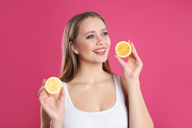 Young woman with cut lemon on pink background. Vitamin rich food