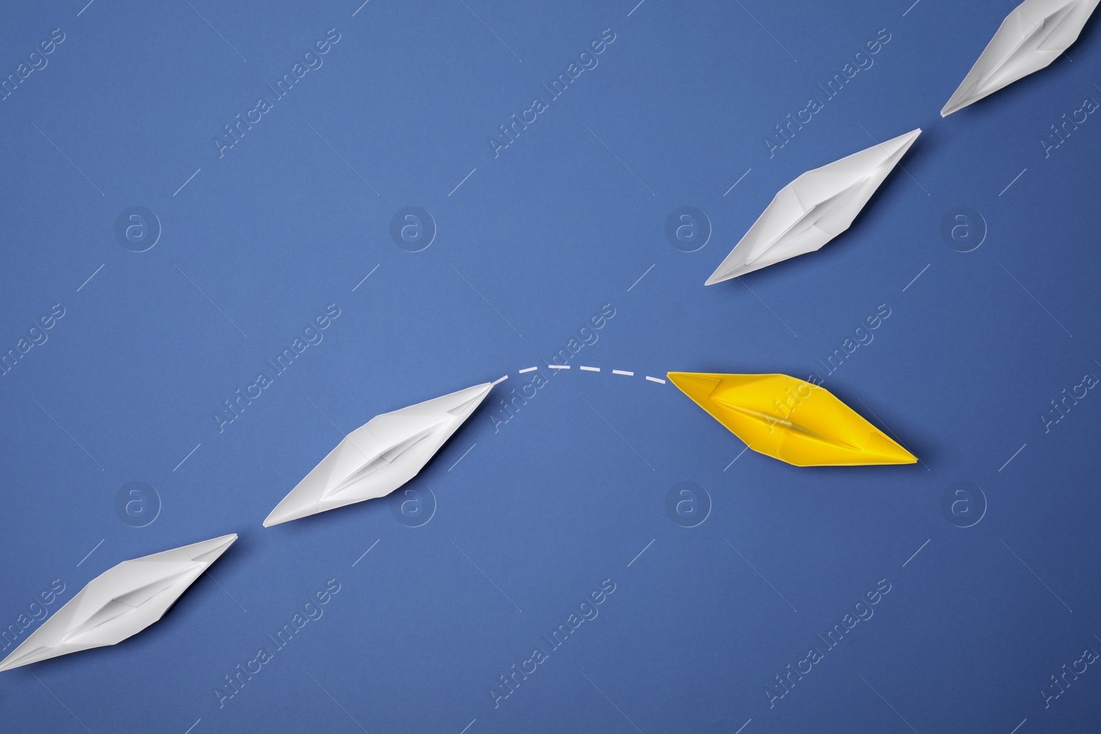 Photo of Yellow paper boat floating away from others on blue background, flat lay with space for text. Uniqueness concept