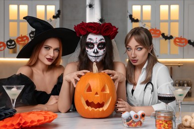 Photo of Group of women in scary costumes with cocktails and carved pumpkin celebrating Halloween indoors