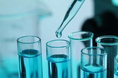 Dripping liquid from pipette into test tube on blurred background, closeup. Laboratory analysis