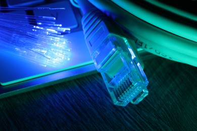 Optical fiber strands transmitting color light near cable with modular connector and computer keyboard on table, closeup
