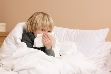 Boy blowing nose in tissue in bed at home. Cold symptoms