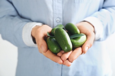 Photo of Woman holding fresh seedless avocados with green leaves, closeup