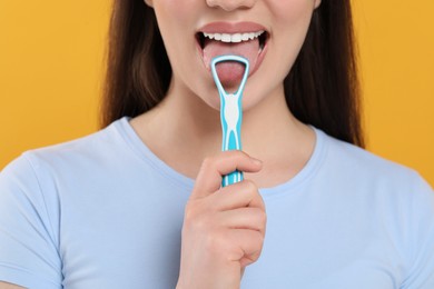Woman brushing her tongue with cleaner on yellow background, closeup