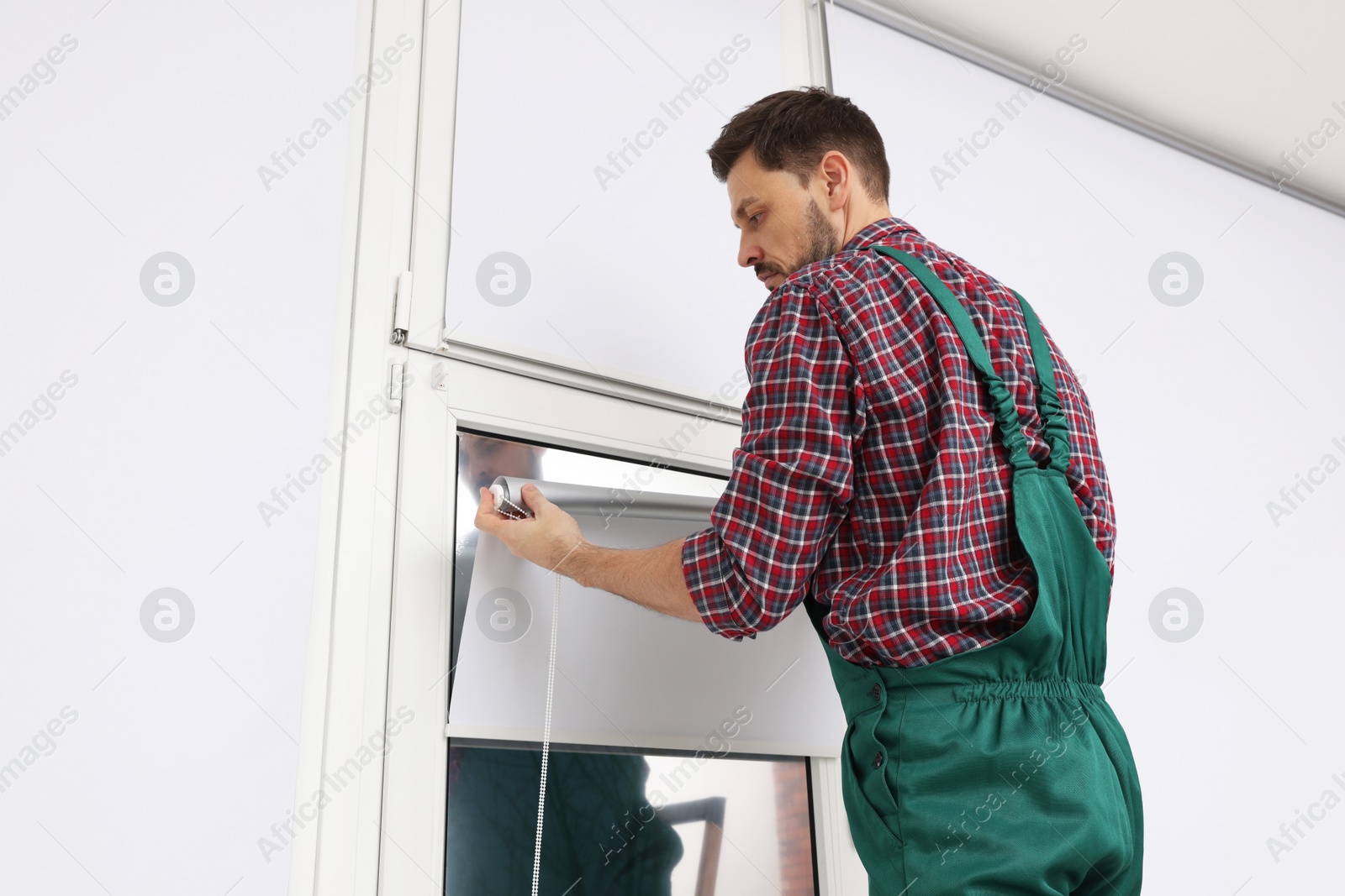 Photo of Worker in uniform installing roller window blind indoors