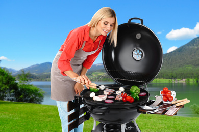 Woman in apron cooking on barbecue grill in park. Picnic time