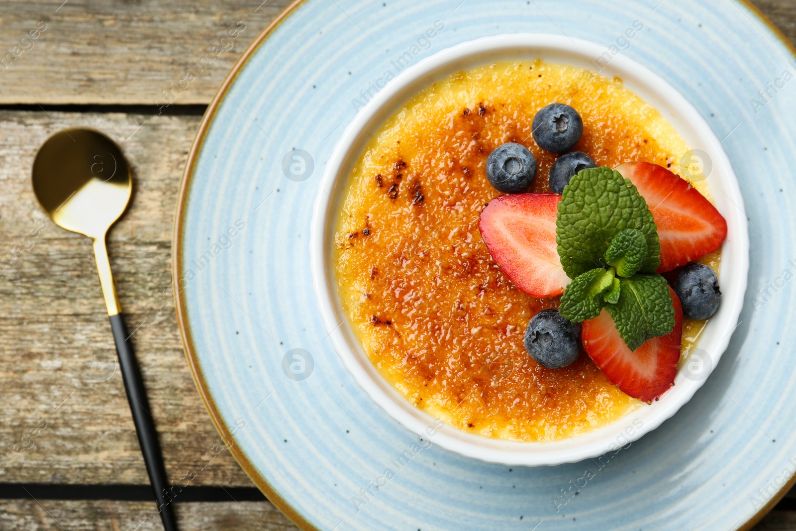 Photo of Delicious creme brulee with berries and mint in bowl served on wooden table, top view