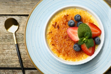 Delicious creme brulee with berries and mint in bowl served on wooden table, top view