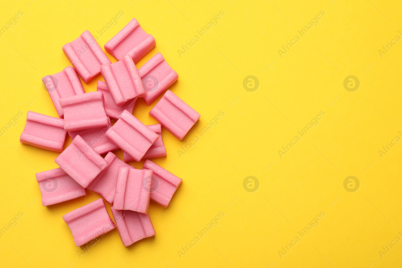 Photo of Tasty pink chewing gums on yellow background, flat lay. Space for text