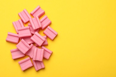 Photo of Tasty pink chewing gums on yellow background, flat lay. Space for text