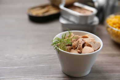 Photo of Bowl of canned tuna with dill on wooden table, space for text