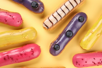 Photo of Delicious eclairs covered with glaze on yellow background, flat lay