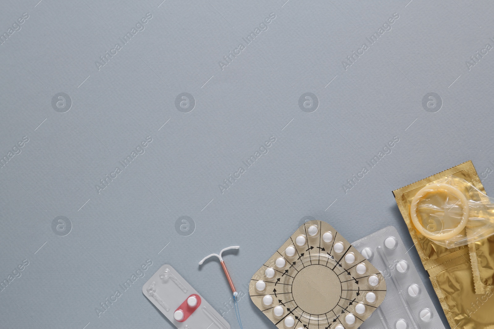 Photo of Contraceptive pills, condoms and intrauterine device on gray background, flat lay with space for text. Different birth control methods