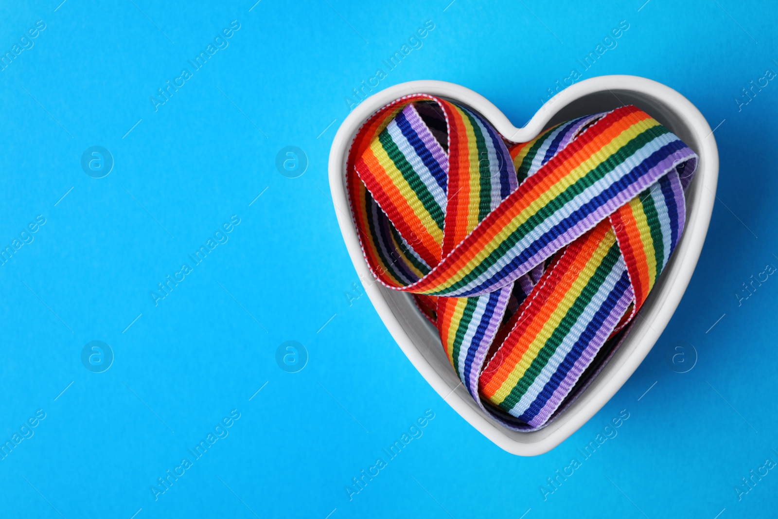 Photo of Heart shaped mold and bright rainbow ribbon on color background, top view with space for text. Symbol of gay community