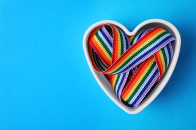 Photo of Heart shaped mold and bright rainbow ribbon on color background, top view with space for text. Symbol of gay community