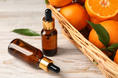Bottle of tangerine essential oil and fresh fruits on white wooden table, closeup