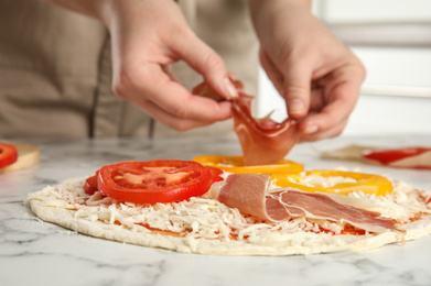 Photo of Woman adding prosciutto to pizza white marble table, closeup