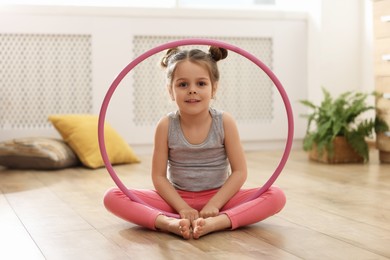 Photo of Little cute girl with hula hoop on floor at home. Doing exercises