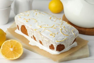Photo of Tasty lemon cake with glaze and citrus fruits on white wooden table, closeup