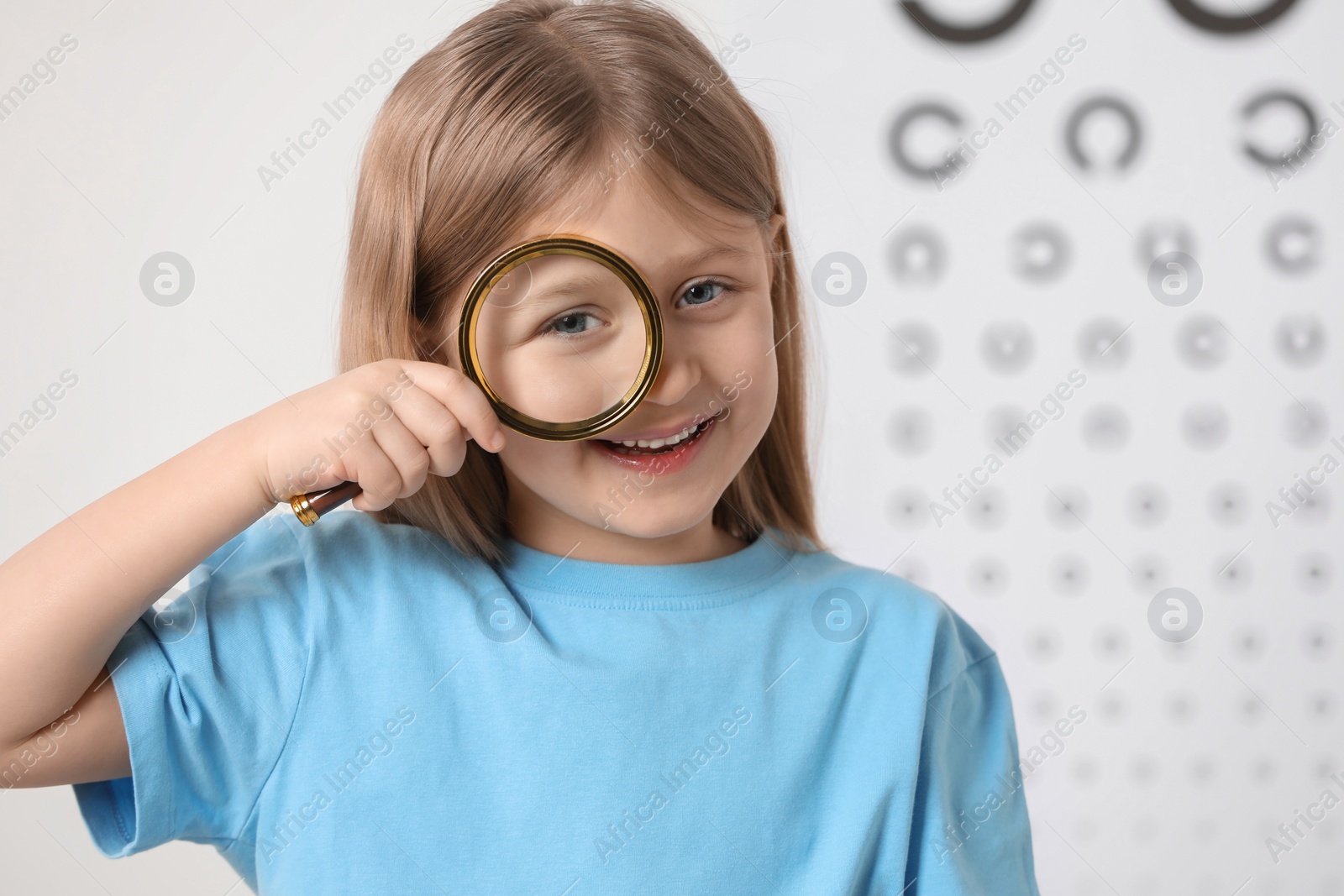 Photo of Little girl with magnifying glass against vision test chart