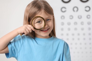 Photo of Little girl with magnifying glass against vision test chart