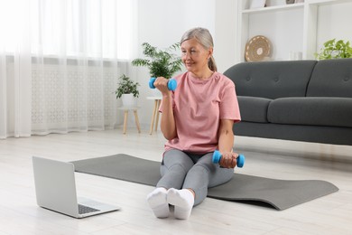 Senior woman exercising with dumbbells while watching online tutorial at home. Sports equipment