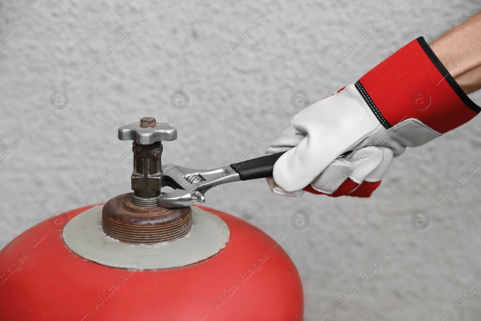 Photo of Worker with adjustable wrench opening red gas cylinder near wall, closeup